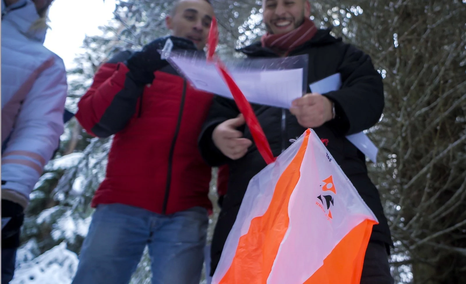 Équipe avec sa carte devant une balise de course d'orientation sur neige
